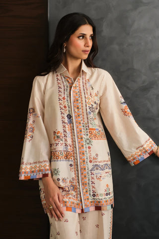 Woman wearing a cream embroidered shirt with colorful patterns against a dark background