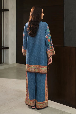 Woman wearing a blue traditional outfit with intricate patterns in a minimal indoor setting.