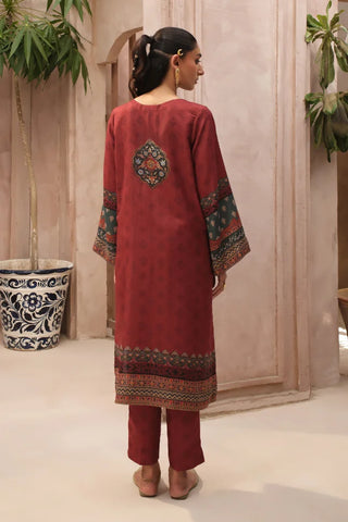 Woman wearing a red traditional outfit with intricate patterns in a minimal indoor setting.